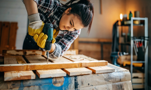 Woman using power drill on wood in a garage