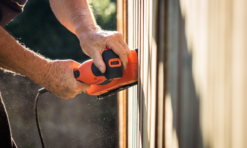 Orange electric sander being used on a wood fence